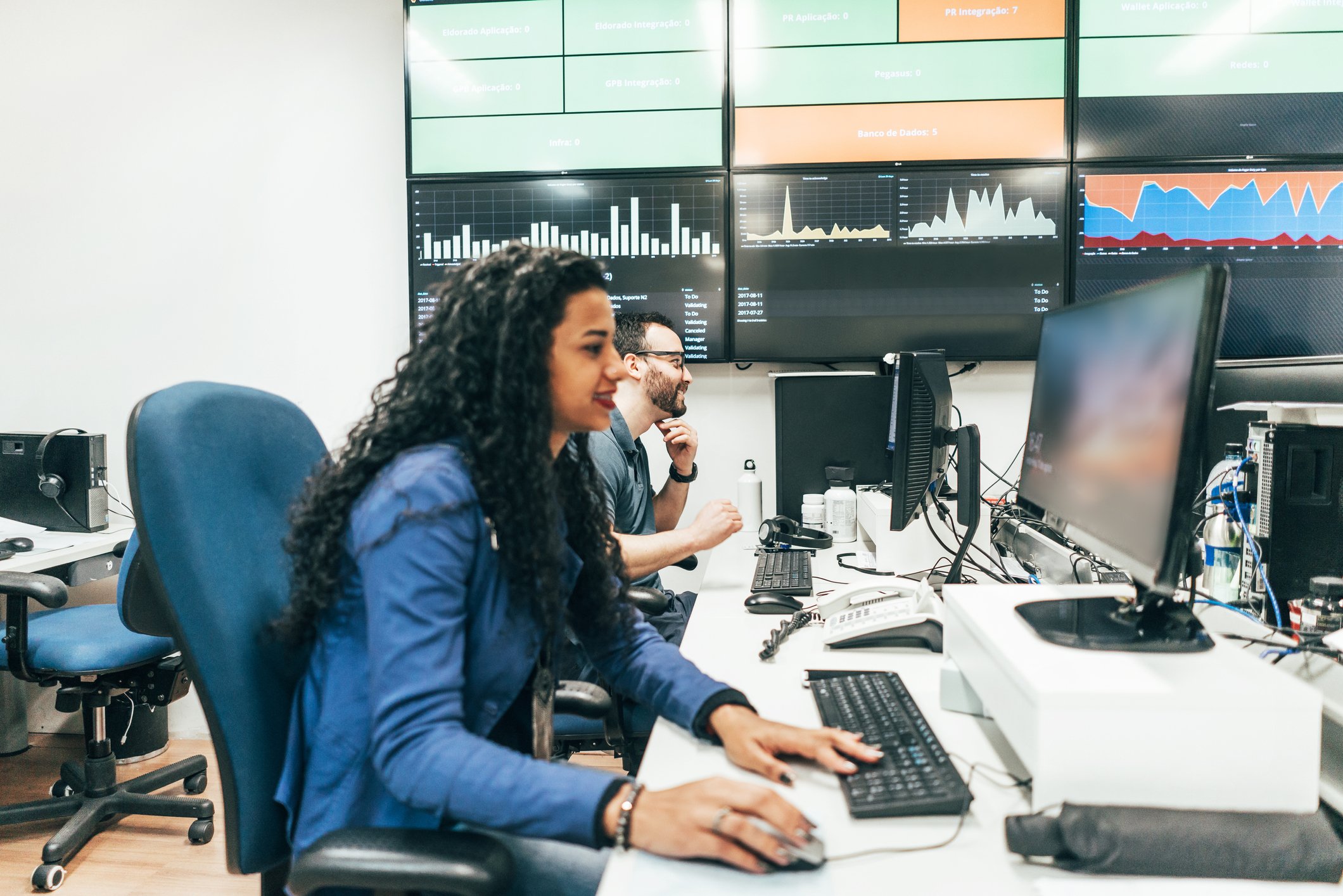 Investors tracking charts on computers and a wall of large screens.