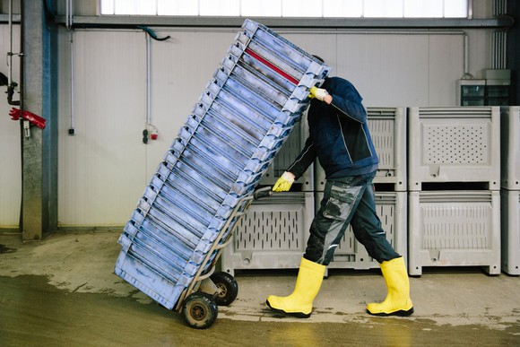 Person pushing cart full of empty containers through a warehouse.