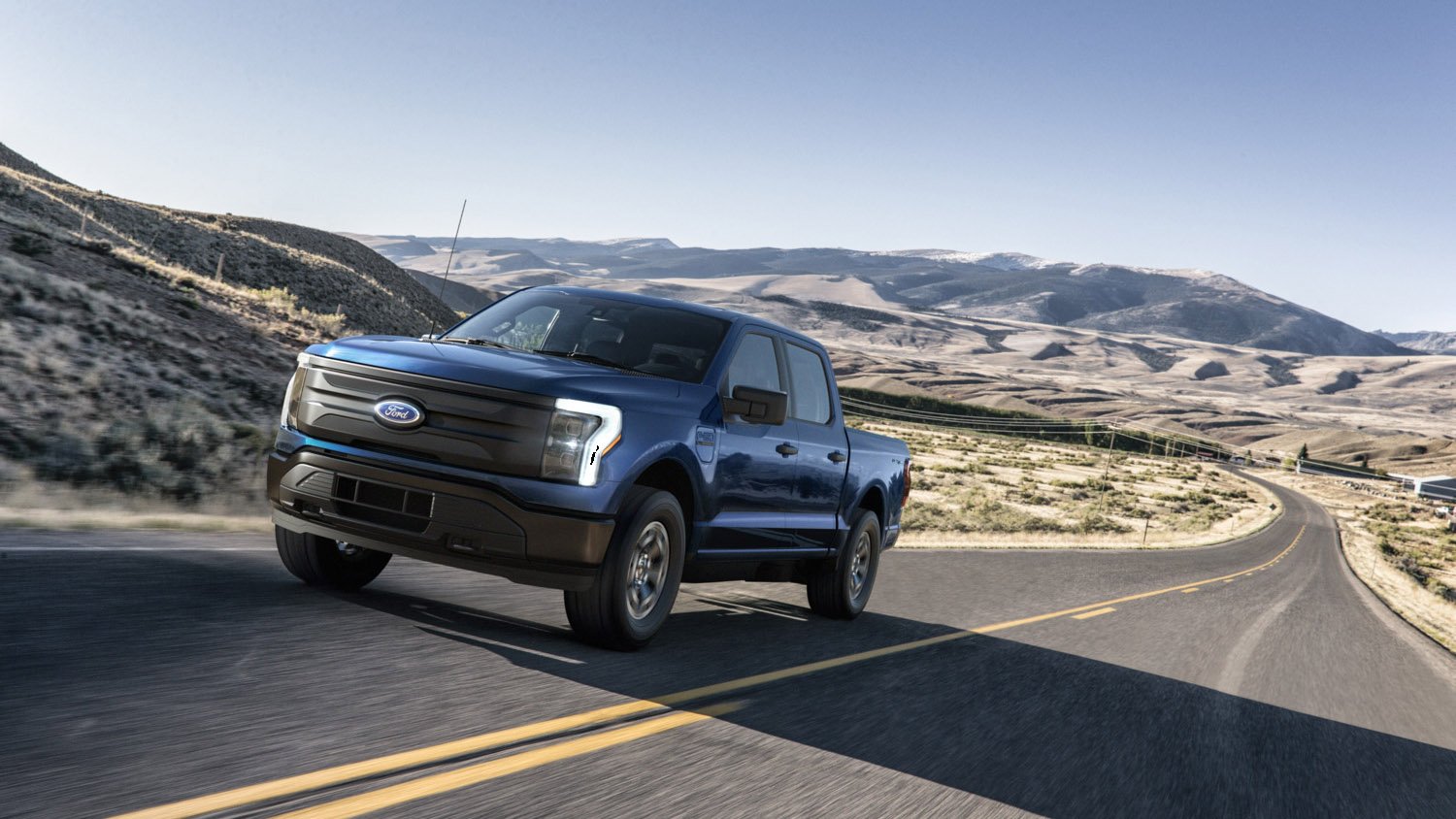 A Ford F-150 Lightning on the highway under a blue sky with mountains in the background.