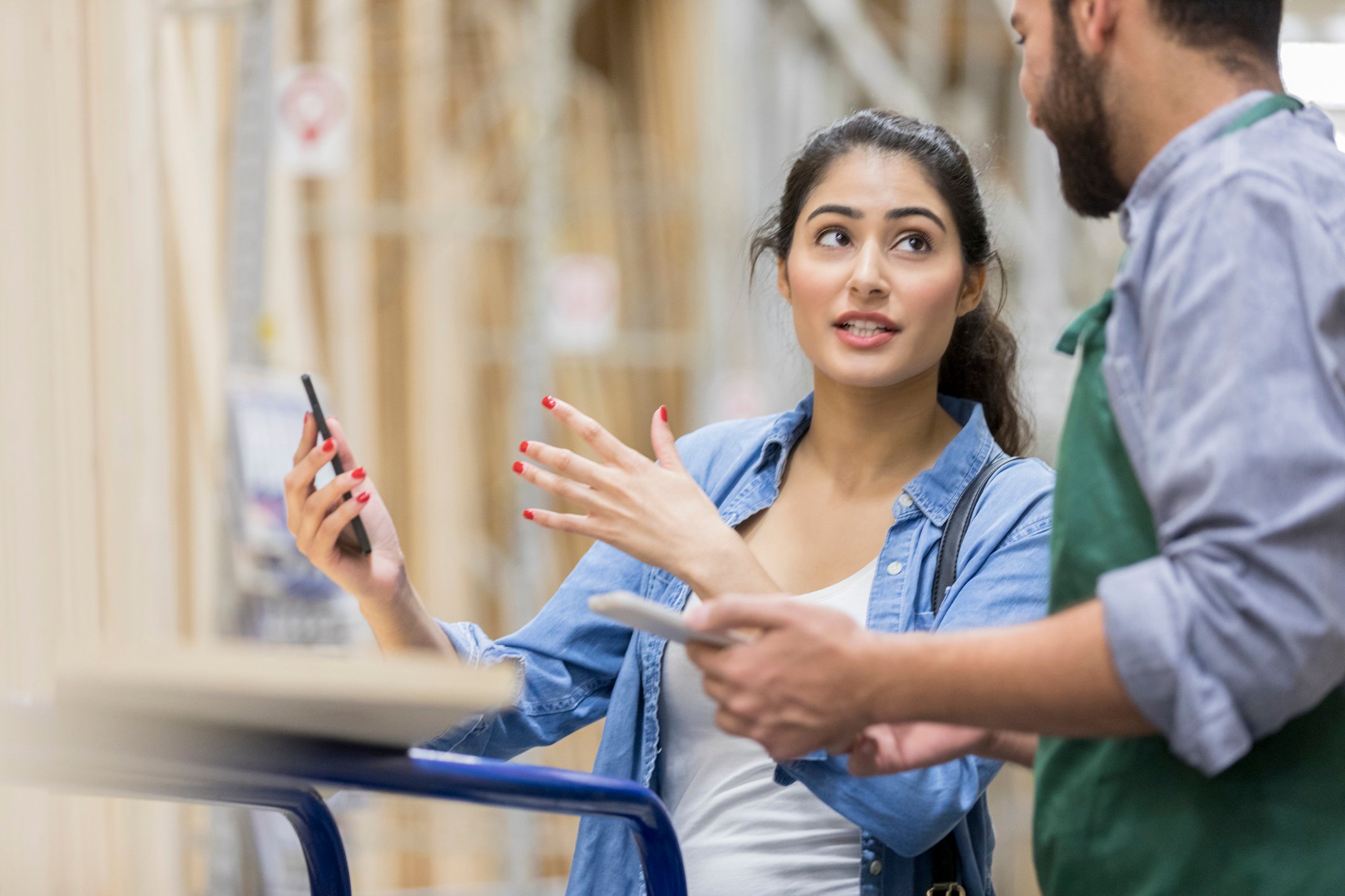 A customer speaks to a store associate in an aisle full of lumber