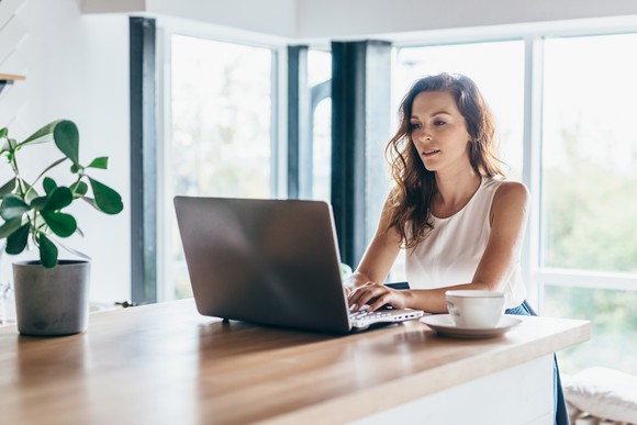 A person using a laptop that's on a kitchen counter.
