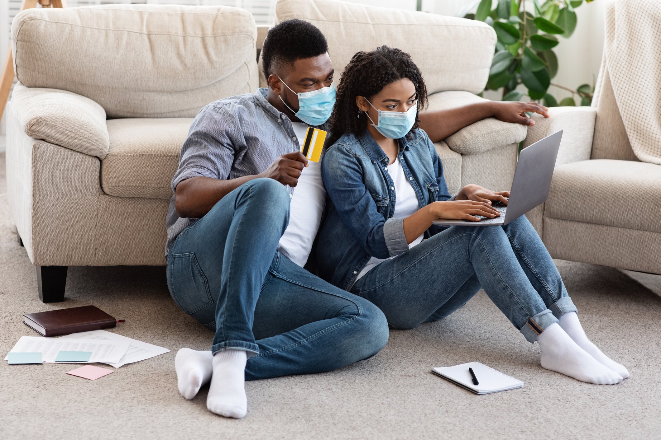 A man and a woman sitting on the floor looking at a laptop.