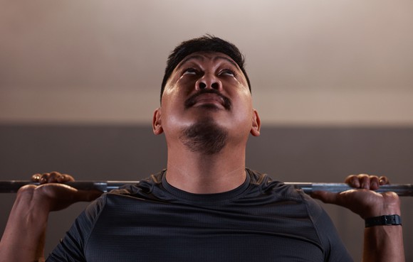 A person is holding a weighted bar and looking up.