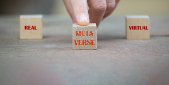 Three small wooden blocks with the words real meta verse and virtual, with a finger moving the middle one. 