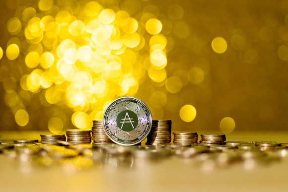 Piles of golden coins with the Cardano logo.