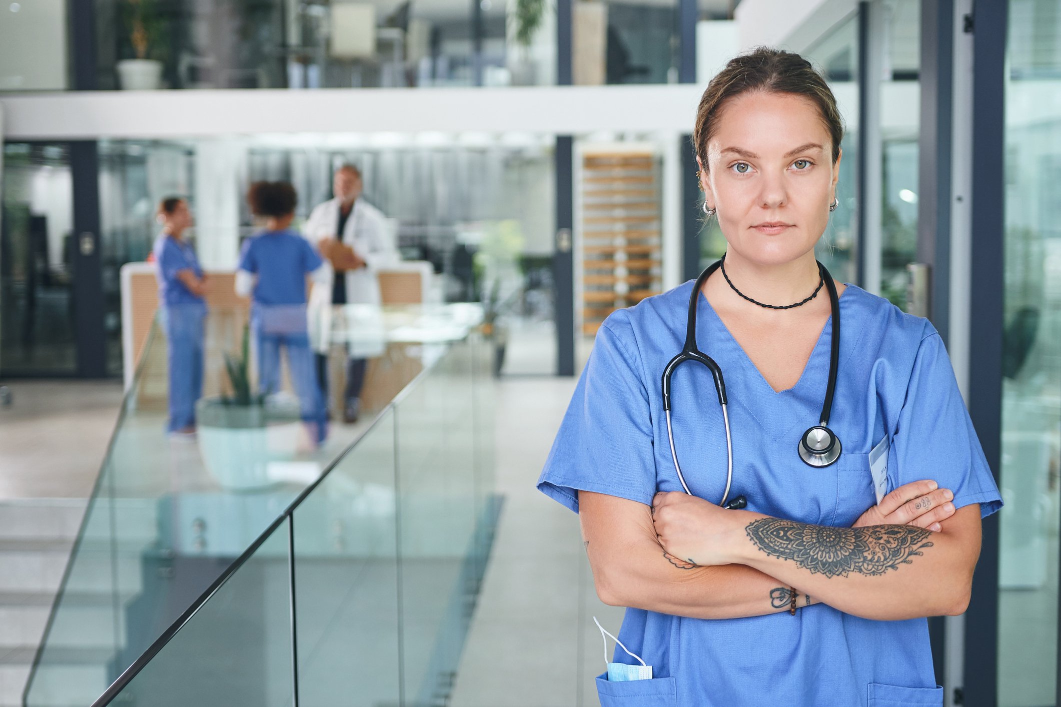 A medical professional with a stethoscope and a tattoo looks determined, with arms crossed.
