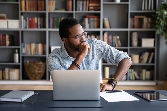 Person at a desk in deep thought, with a floor-to-ceiling bookcase in the background.