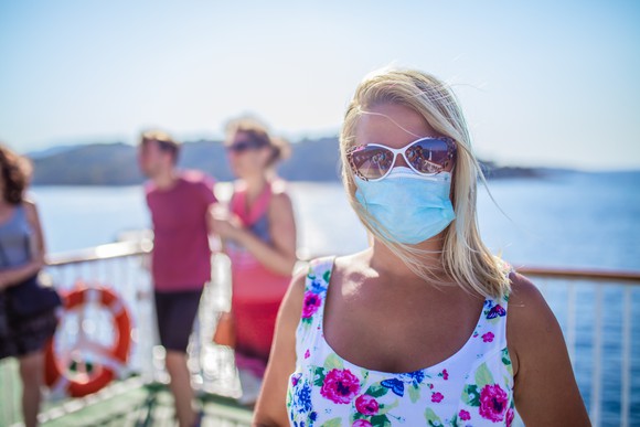 Person poses on the deck of a cruise ship while wearing a face mask.