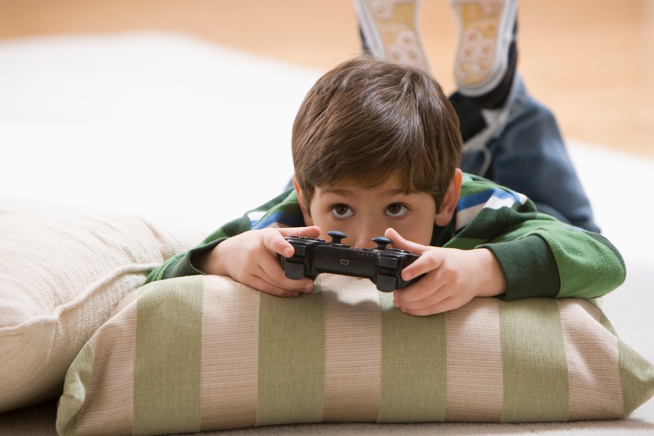 A young child laying on the floor while playing a video game.