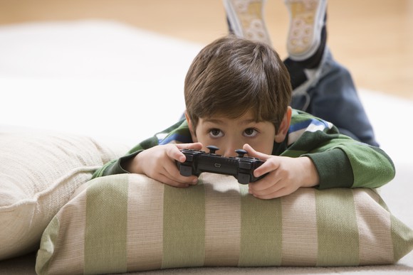A young child laying on the floor while playing a video game.