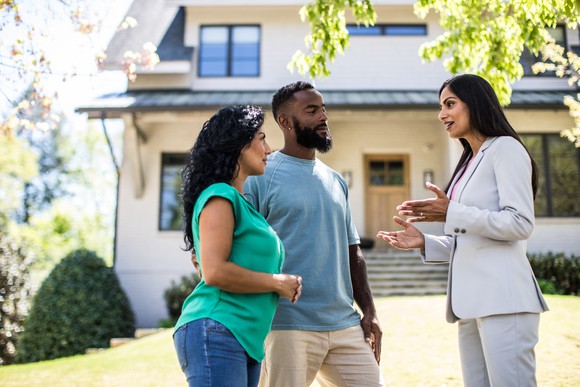 People meet with a real estate agent in front of a house.