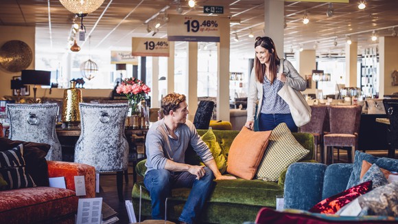 Two people check out a couch and pillows in a home goods store.