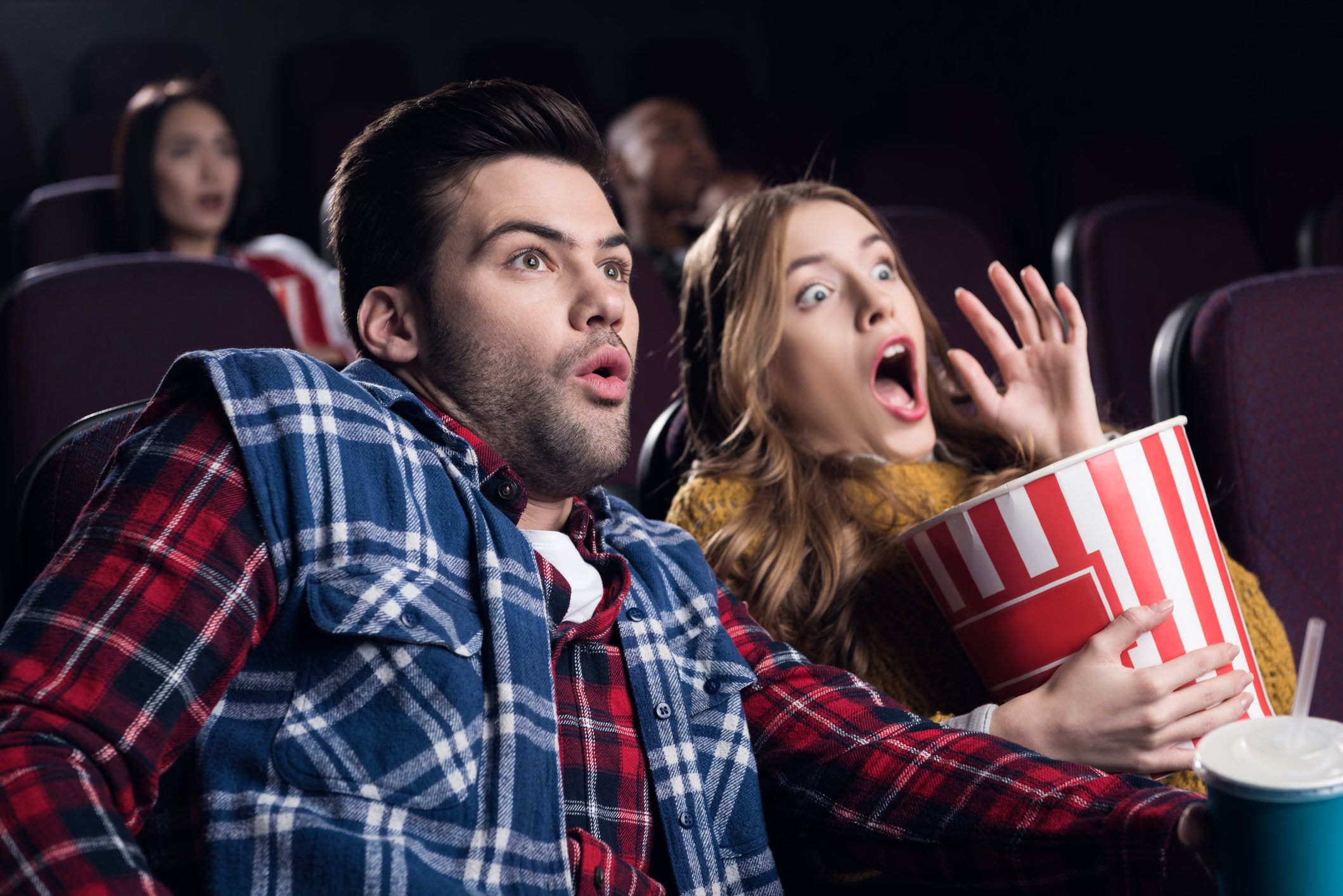 Two people watching a scary movie at theater.