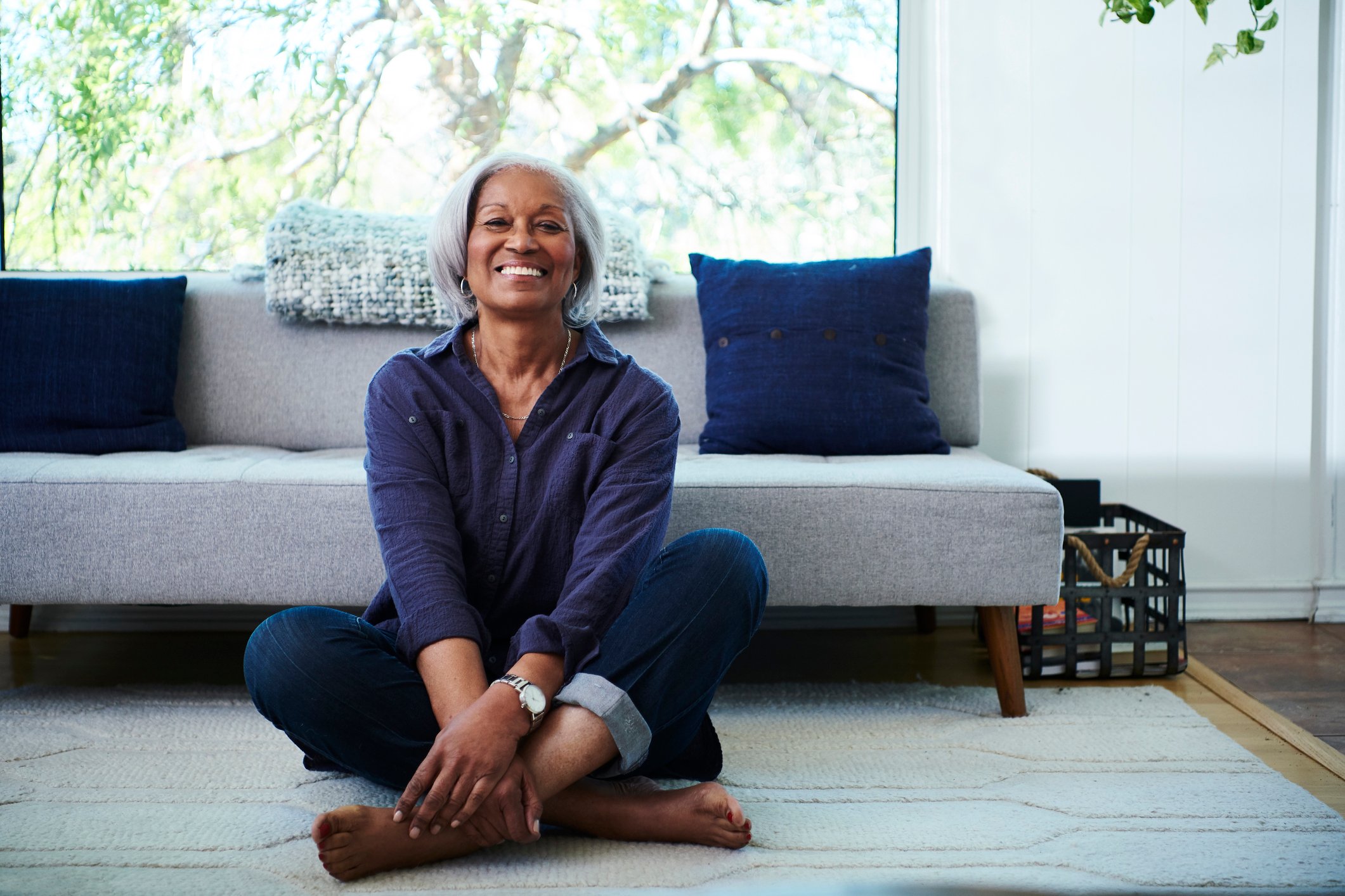 Smiling senior sits on the floor, cross-legged, at home.