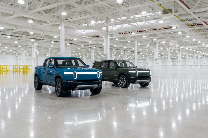 Rivian R1T pickup and R1S SUV on well-lit factory floor. 