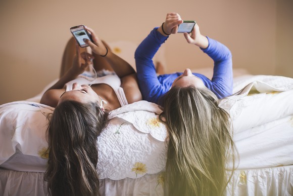 Two people looking at their phones on a bed.