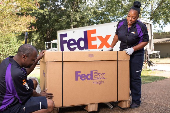 Two FedEx employees carrying a box.