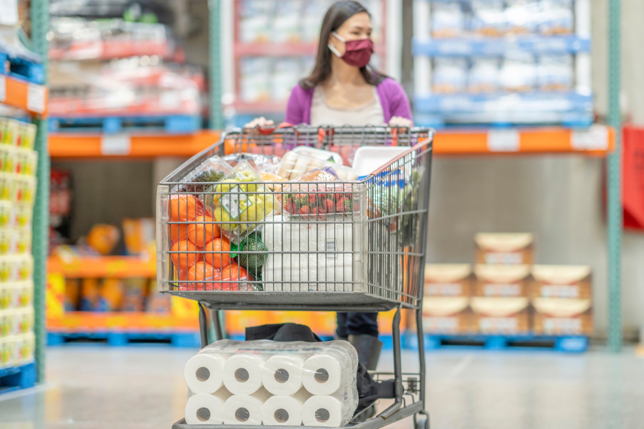 A masked shopper pushes a full cart through a grocery store.