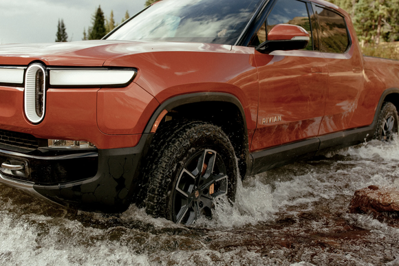 Rivian's R1T pickup truck is driving through a creek.  