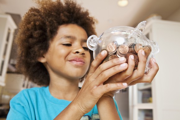 A child checks a glass piggy bank filled with pennies.