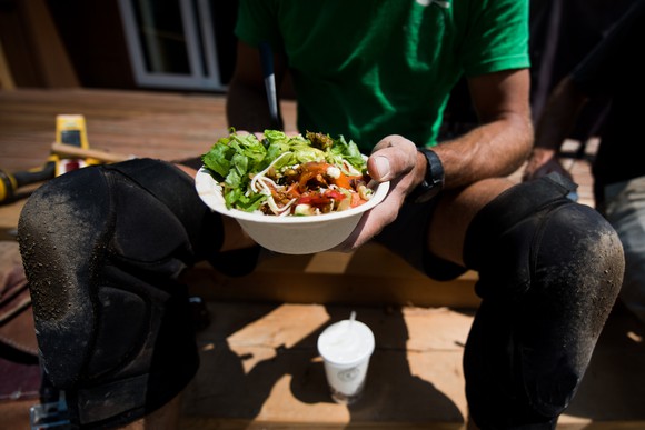 Person sitting and enjoying a bowl of fast casual food with a drink.