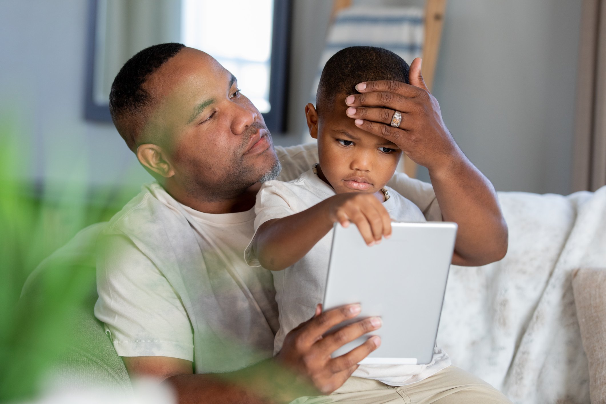 An adult places his hand on a child's forehead during a telemedicine visit.
