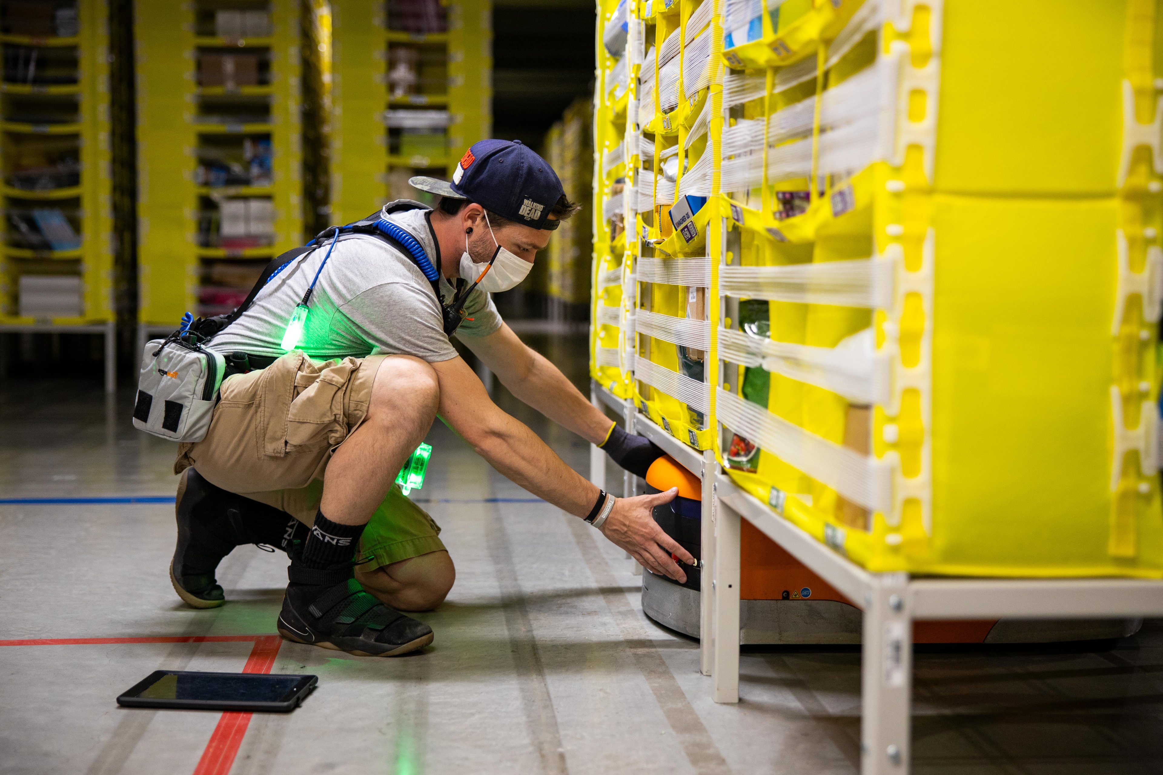 Amazon warehouse worker adjusting a robot under a shelving unit.