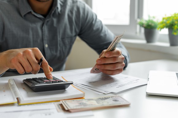 A person at a desk using a calculator while making notes on financial statements.