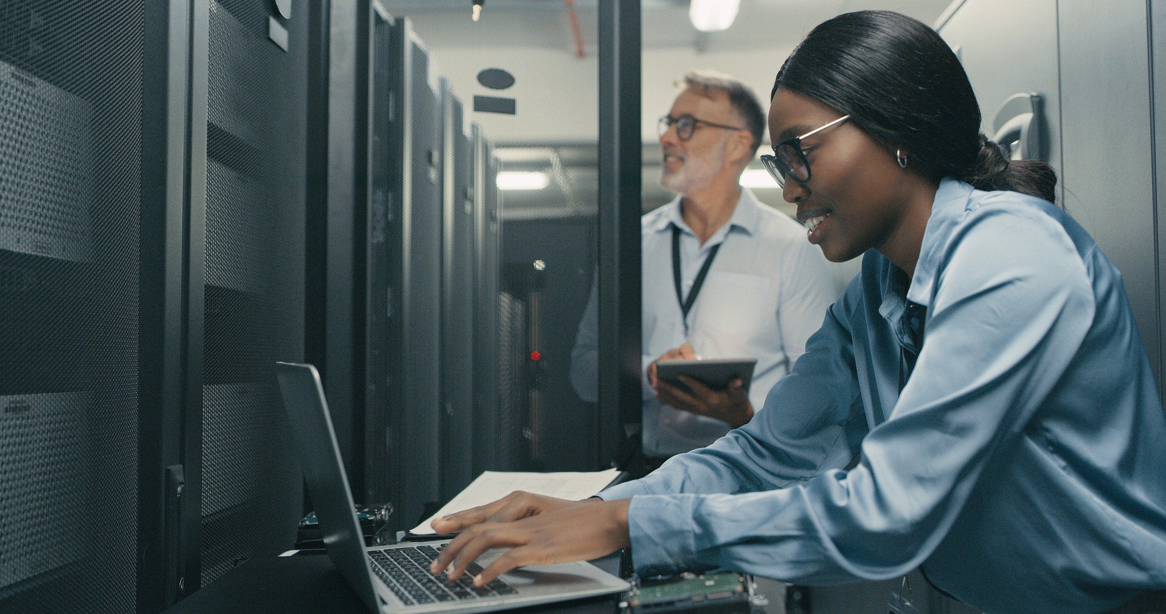 A worker uses a laptop while investigating an issue on a server farm.