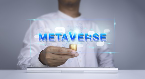 A person holding a stack of gold coins near a glass panel with "Metaverse" printed on it.