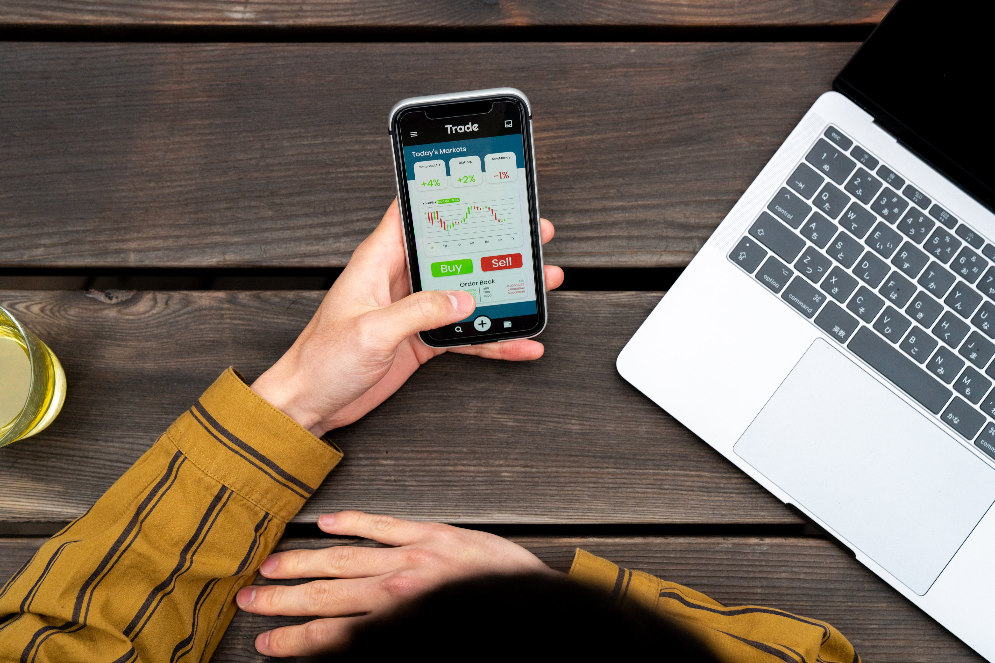 A person sitting at a desk trading stocks on a smartphone.