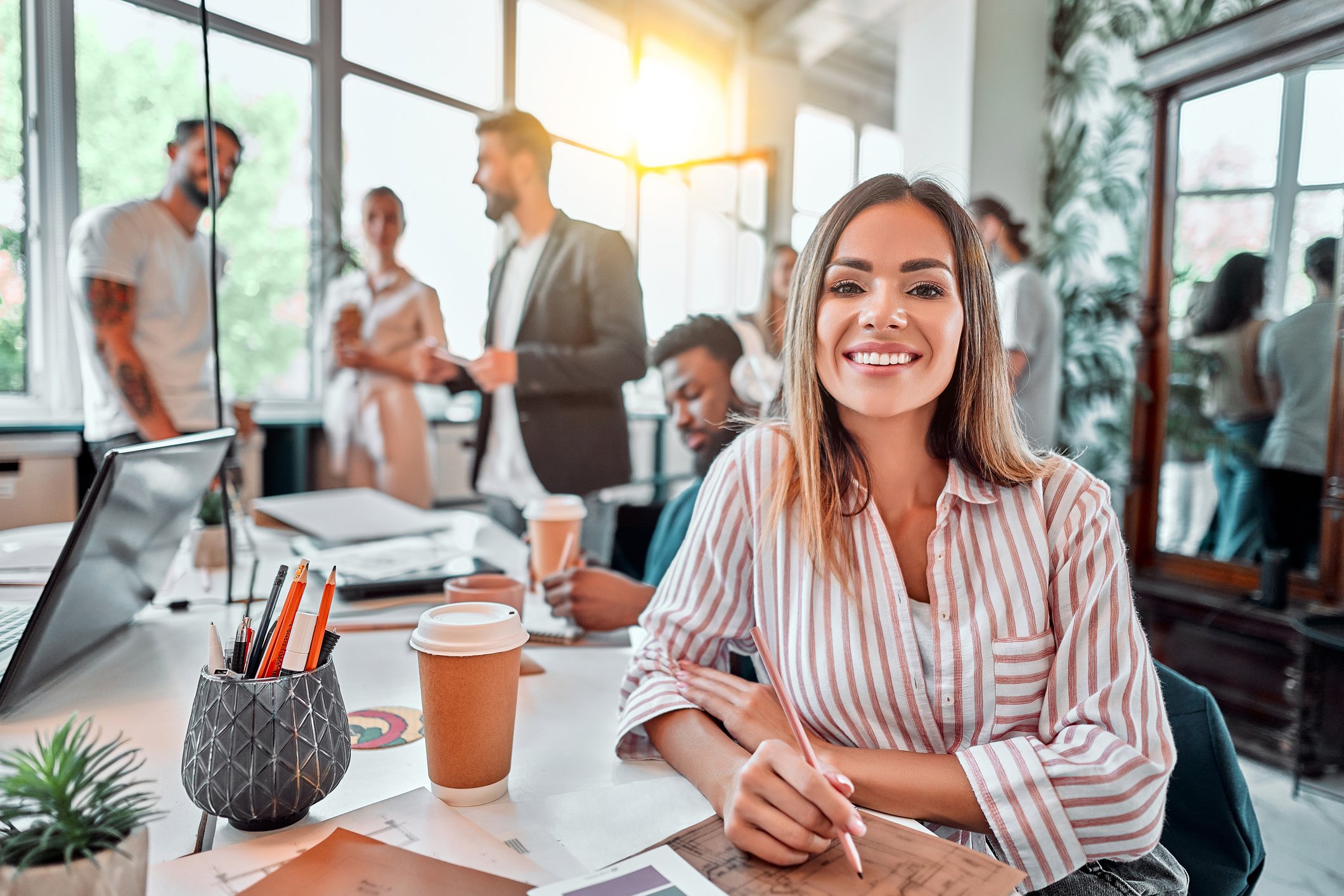 Smiling office worker sitting at desk with paperwork and coffee.