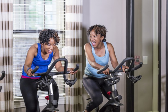 Two people smiling on exercise bikes.