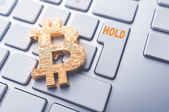 Bitcoin symbol in gold, atop a keyboard featuring a HOLD key.