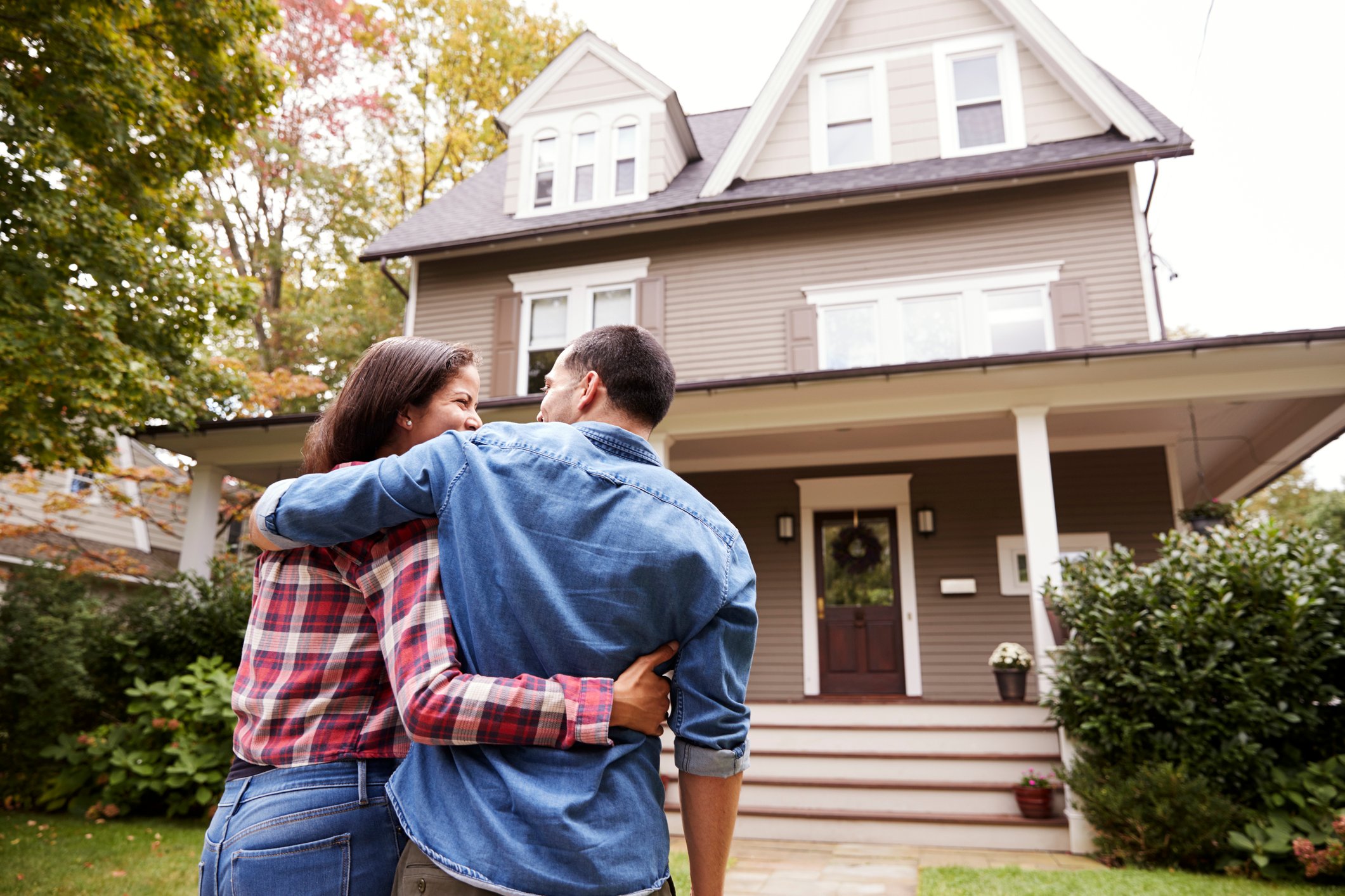 Two people holding each other facing a house.