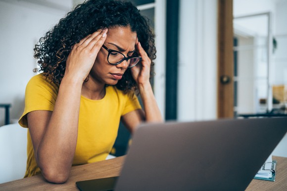 Confused person with hands on their temples looking at laptop.