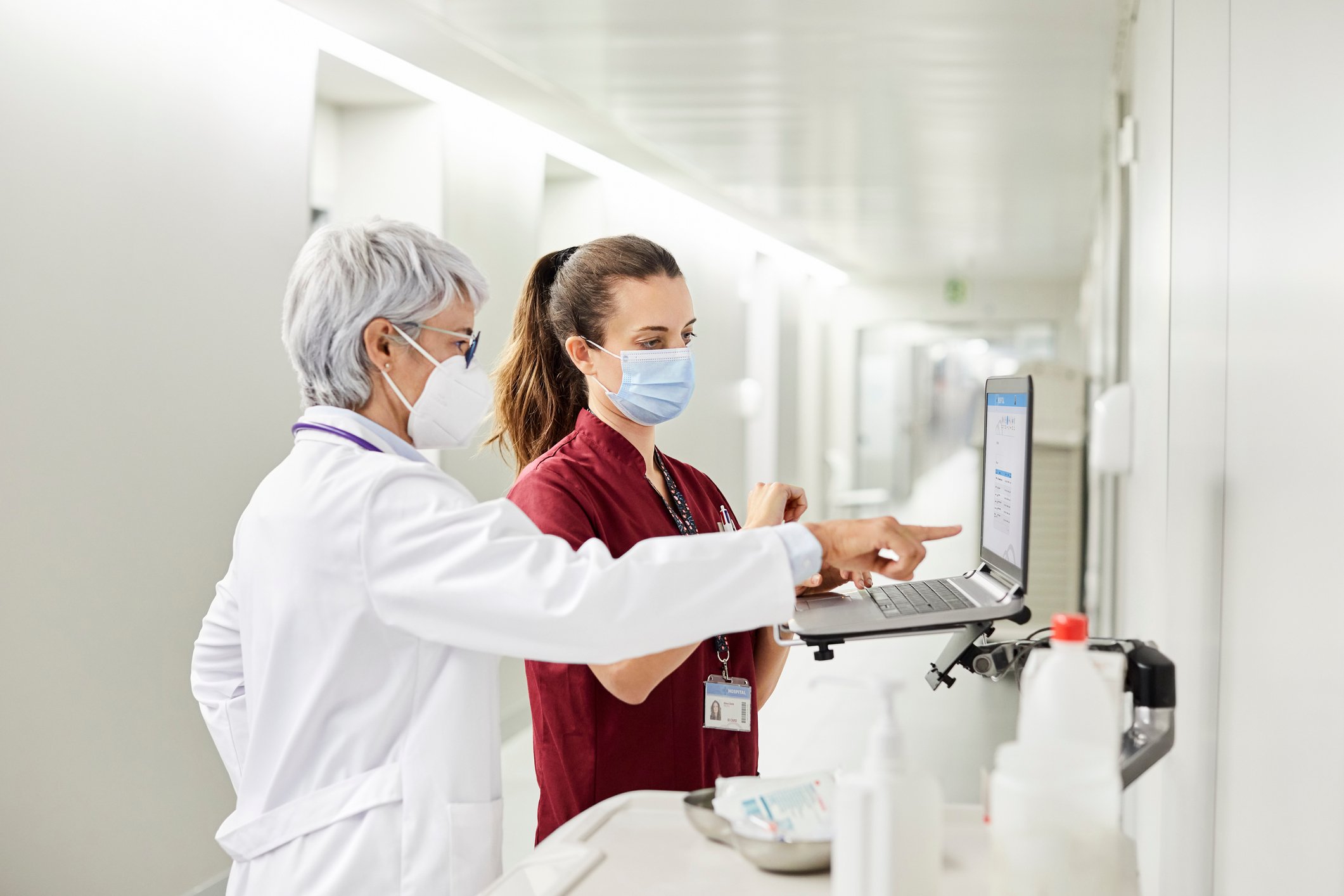 Physician and nurse in a hospital who are wearing masks and looking at a computer screen.