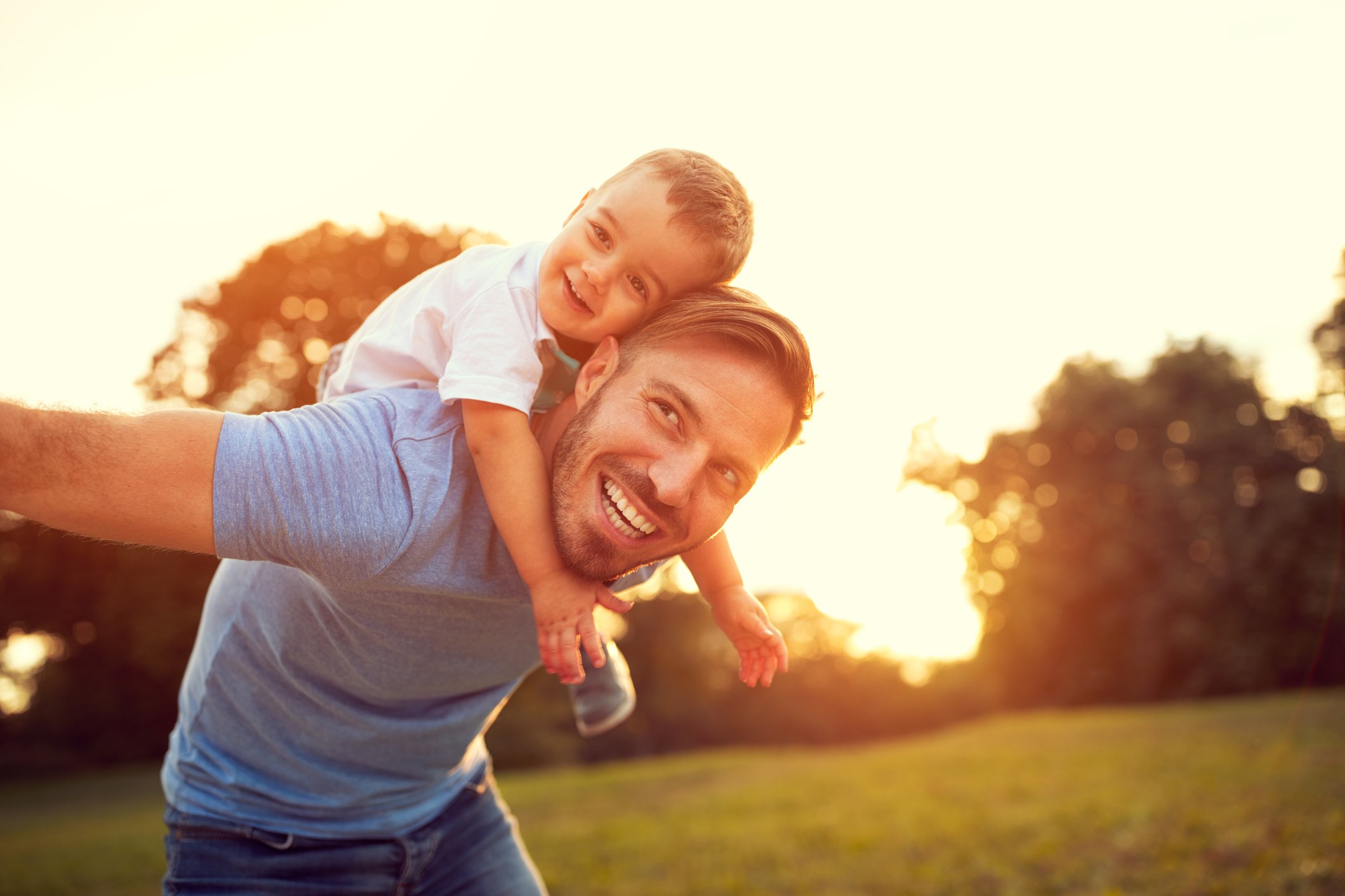 Adult smiles while giving smiling child a piggyback ride outside.