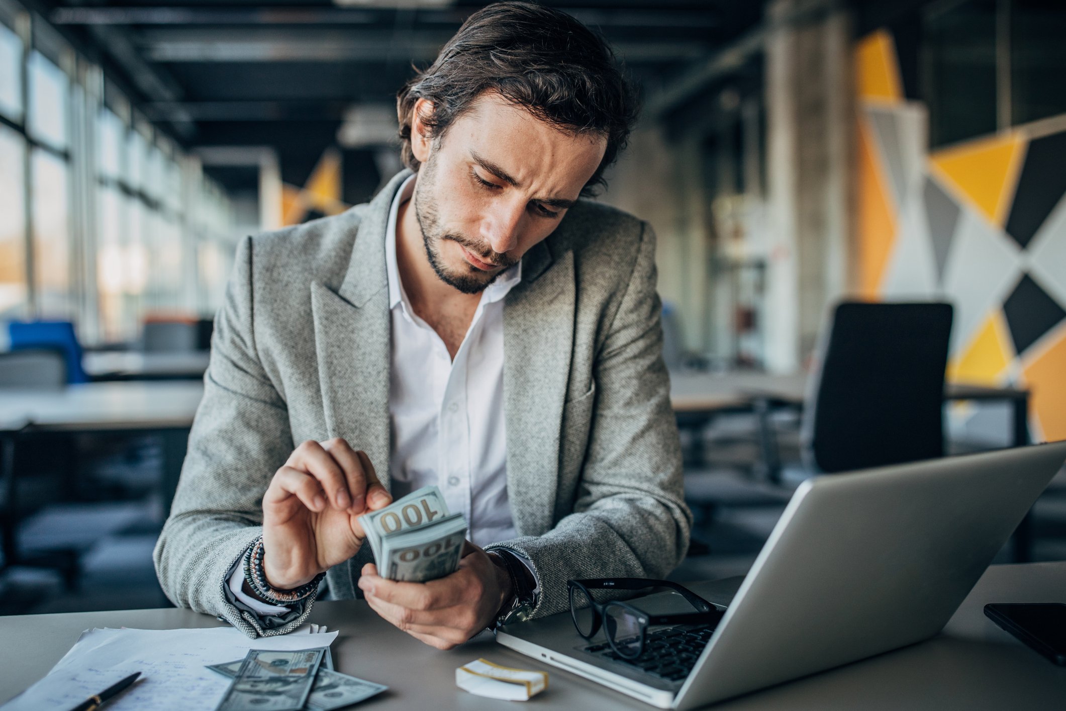 Person wearing a suit holding a stack of hundred dollar bills while counting at a desk. 