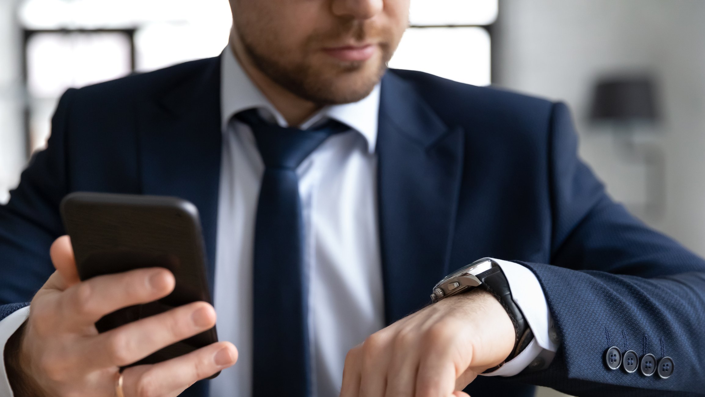 A person holding a smartphone and looking at a wristwatch.