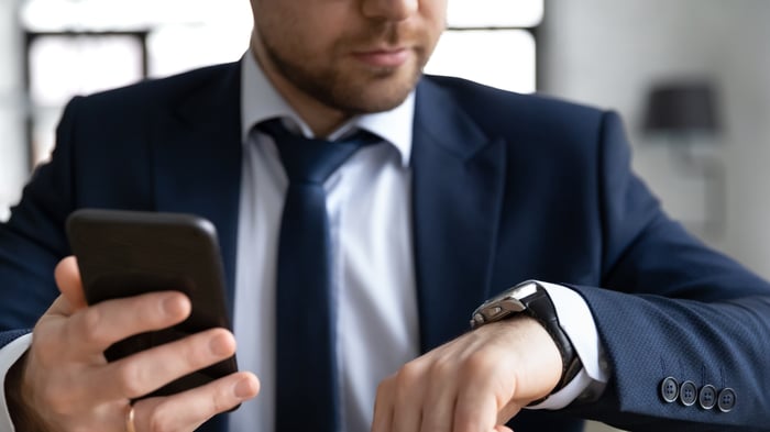 A person holding a smartphone and looking at a wristwatch.