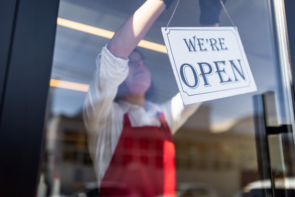 Person hanging "we're open" sign in a store window.