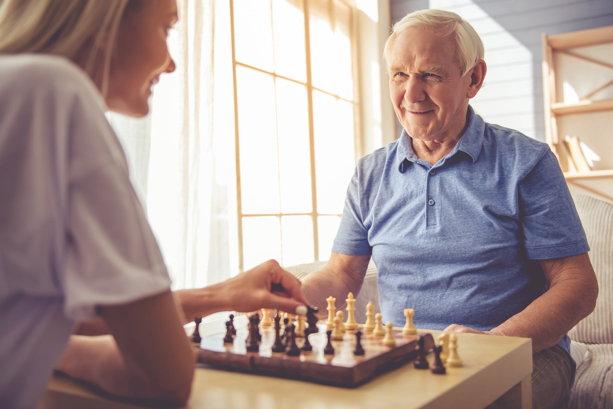 Retired people smiling and playing chess at a table.