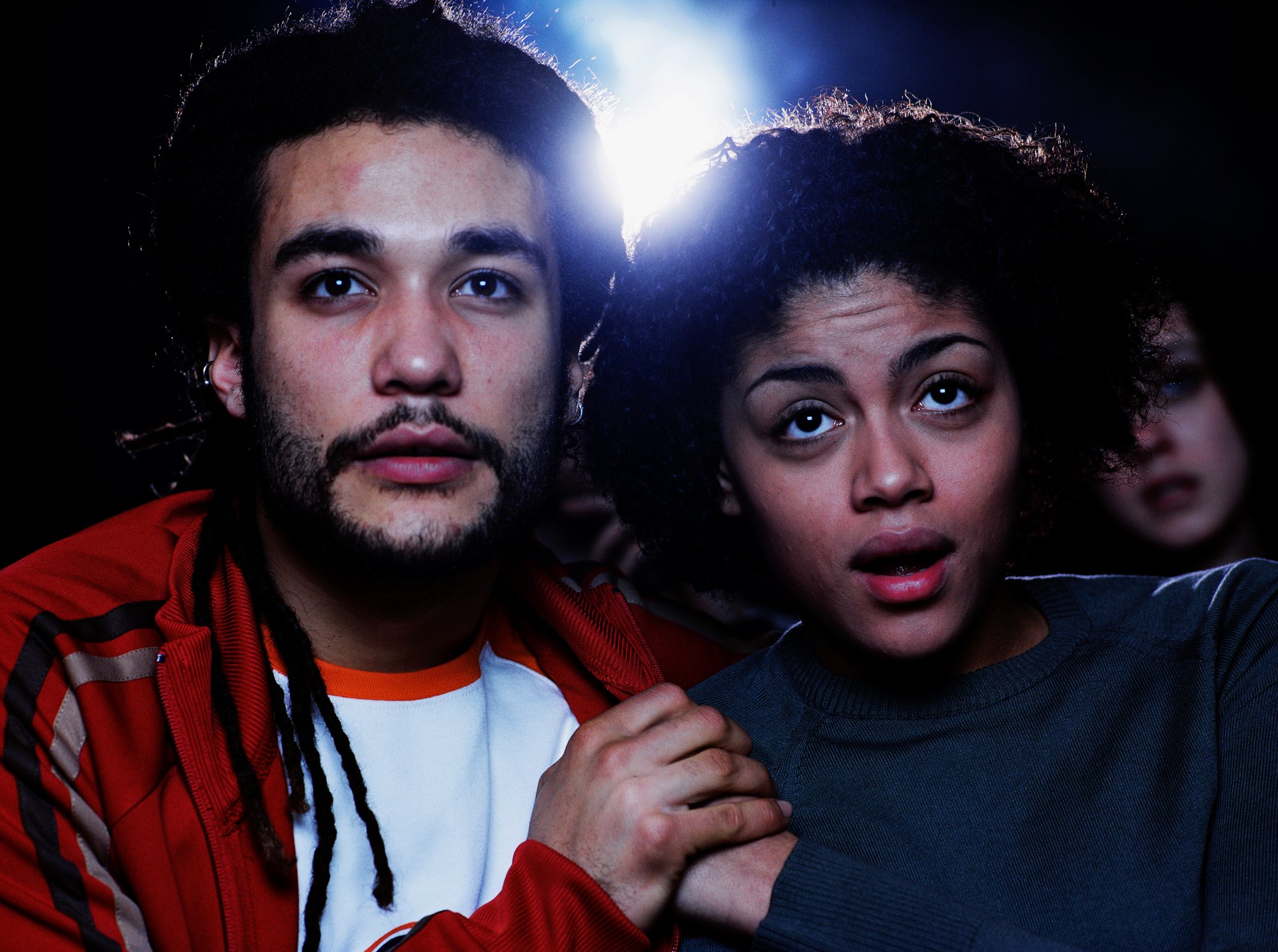 Two people holding hands at a movie theater, mesmerized by what is being projected on the big screen.