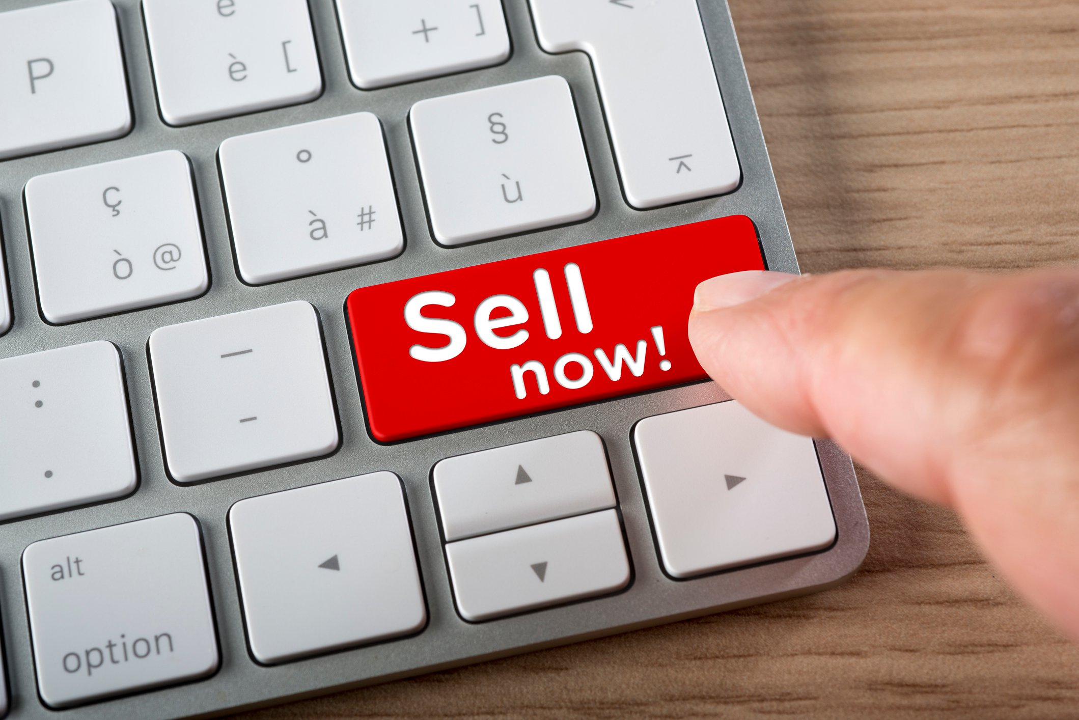 A finger pressing a bright red keyboard button that says Sell Now.