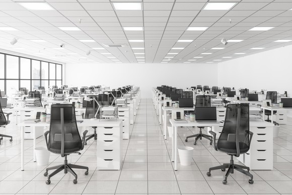 Numerous chairs and desks sit lined up in an empty office space