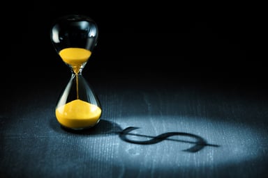 An hourglass casting a dollar-sign shadow.