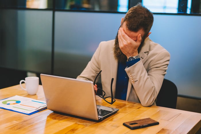 A person sits in front of a computer, covering their eyes.