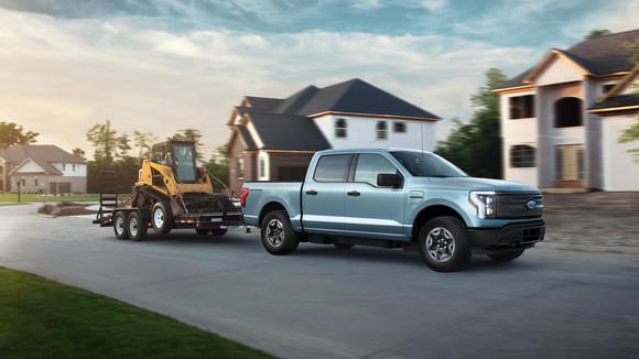 Ford F-150 Lightning towing heavy equipment in a residential neighborhood.