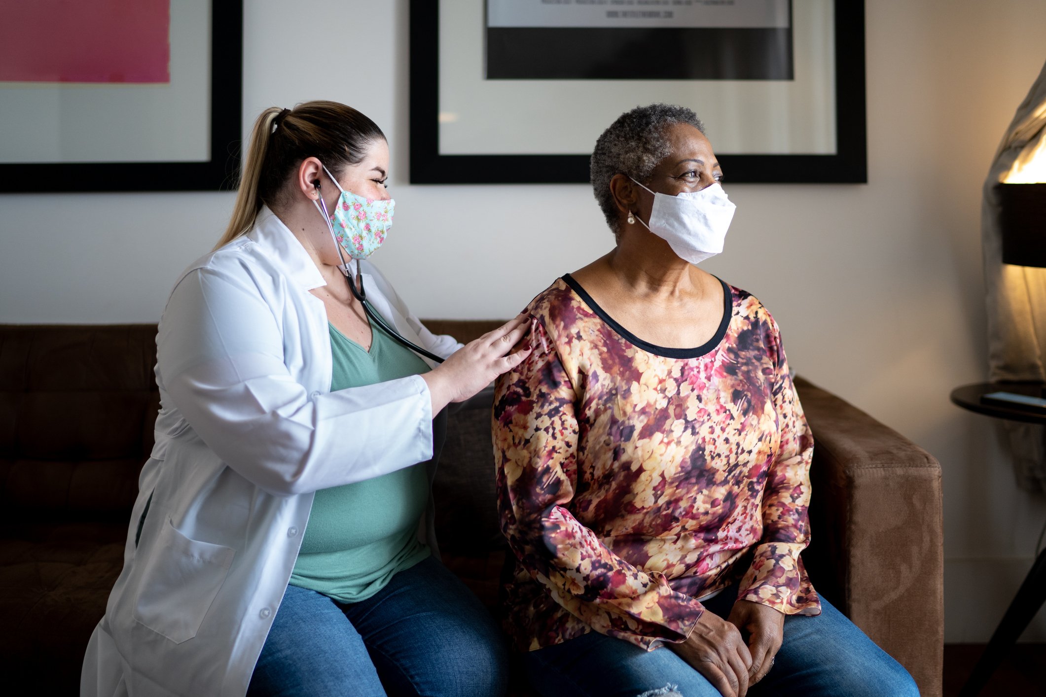 A masked healthcare practitioner checking a masked patient with a stethoscope.